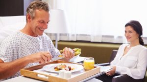 homem na cama de hospital, sorrindo e se alimentando